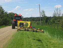 A large mower pulled by a tractor along the side of a road